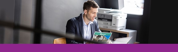 Mies istuu työpisteessään värillinen asiakirja kädessään