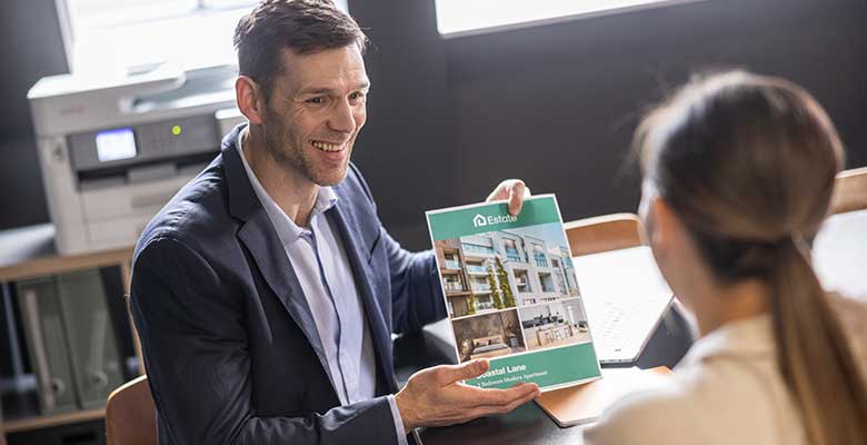 Mies esittelee asiakkaalle värillistä A4-esitettä