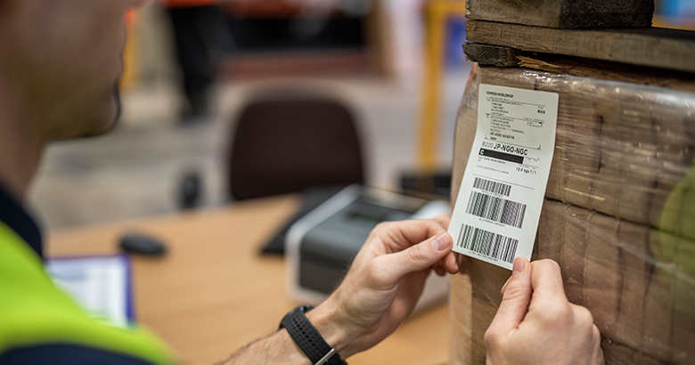 Työntekijä kiinnittää Brotherin lämpötulostimella tulostettua viivakooditarraa pakettiin